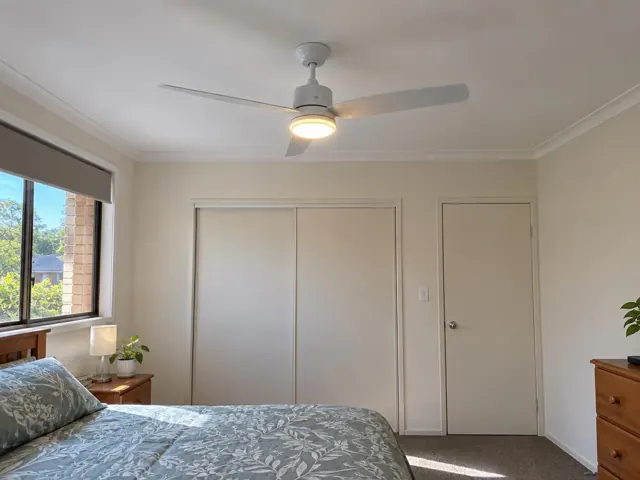 Ceiling fan installed in a beige bedroom with window, closet doors and carpet in Gillieston Heights